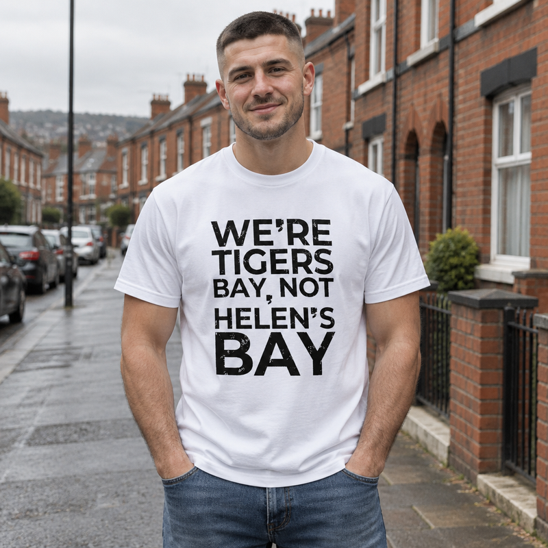 Man wearing the white We're Tigers Bay, Not Helen's Bay tee on a red brick street in North Belfast