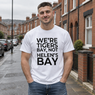 Man wearing the white We're Tigers Bay, Not Helen's Bay tee on a red brick street in North Belfast